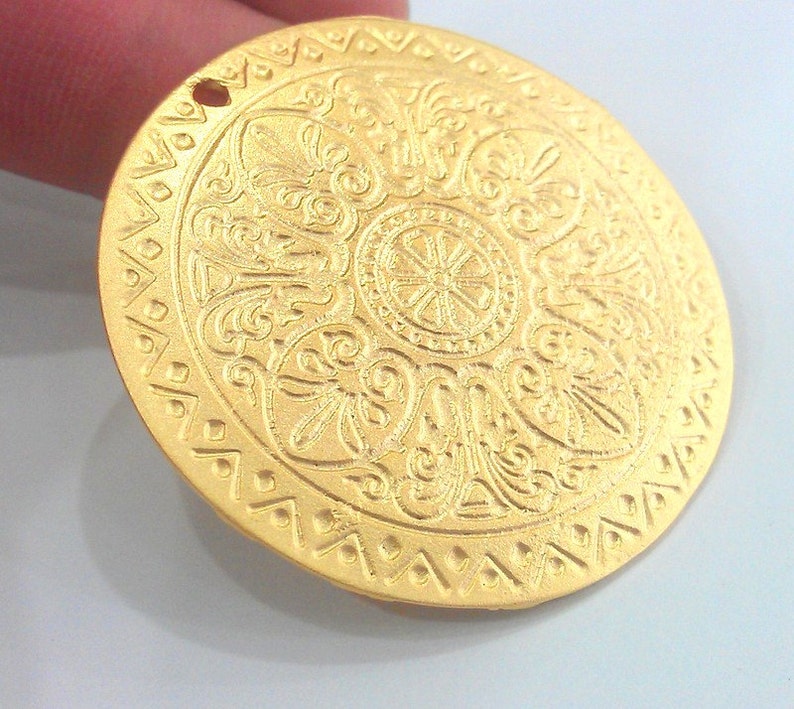 Peut inclure: Un pendentif en m&eacute;tal dor&eacute; avec un motif circulaire complexe. Le pendentif a un trou en haut pour l'accrocher.