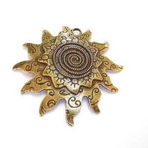 K&ouml;nnte beinhalten: Ein goldfarbener Metall-Sonnenanh&auml;nger mit einem detaillierten Spiraldesign in der Mitte und filigranen Ranken an den R&auml;ndern.