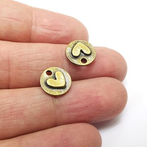 May include: Two antique gold-toned metal charms with a heart design. Each charm has a hole for attaching to a necklace, bracelet, or other jewelry.
