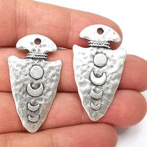 May include: Two silver arrowhead charms with a textured surface and a crescent moon design. Each charm has a small hole at the top for attaching to jewellery.