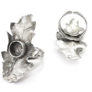 Puede incluir: Un anillo de plata con un diseño de hoja de roble. El anillo tiene una abertura redonda en el centro de la hoja, que se puede utilizar para sujetar una pequeña piedra u otro adorno.
