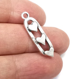 Op de afbeelding: Zilveren bedel met drie hartvormige uitsparingen. De bedel is langwerpig en heeft een lus aan de bovenkant om aan een ketting of armband te bevestigen.