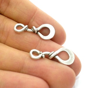May include: Two silver metal clasps with a twisted wire design. The clasps are in the shape of a loop with a smaller loop on one end.
