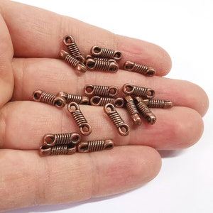 Peut inclure: Un tas de joncs de saut en métal de couleur cuivre, également appelés anneaux fendus, de différentes tailles. Ces anneaux sont utilisés pour relier des composants de bijoux, tels que des chaînes, des breloques et des pendentifs.