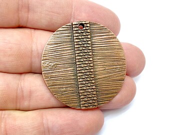 May include: A round copper pendant with a textured design. The pendant has a vertical stripe of a different texture down the center.