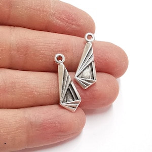 Puede incluir: Dos colgantes de plata con un diseño geométrico. Los colgantes tienen forma de lágrima y presentan un patrón repetitivo de triángulos.