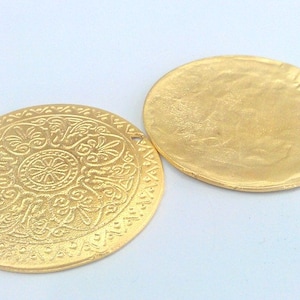 Peut inclure: Deux pendentifs ronds en m&eacute;tal de couleur dor&eacute;e. Un pendentif a un motif en relief d&eacute;taill&eacute; et l'autre est lisse.