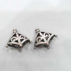 May include: Two silver filigree pendant caps with a decorative design. The caps are square shaped with a pointed top and have a hole at the top for attaching a chain or cord.