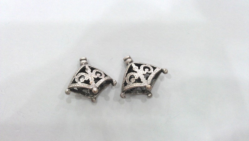 May include: Two silver filigree pendant caps with a decorative design. The caps are square shaped with a pointed top and have a hole at the top for attaching a chain or cord.