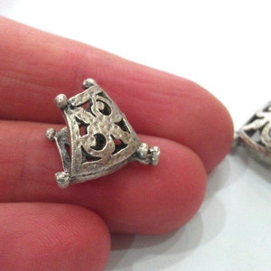 May include: Two silver-toned metal pendant caps with an intricate, openwork design. The caps are triangular in shape and have a delicate, filigree pattern.