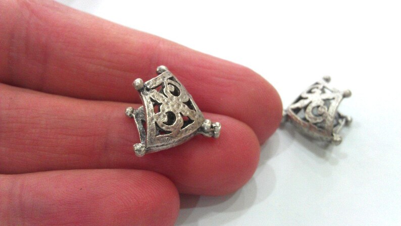 May include: Two silver-toned metal pendant caps with an intricate, openwork design. The caps are triangular in shape and have a delicate, filigree pattern.