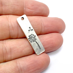 May include: Silver charm with a dandelion design. The dandelion has a stem and seeds that are blowing in the wind. The charm has a hole at the top for attaching to a necklace or bracelet.