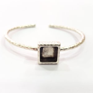 Puede incluir: Pulsera de plata con un bisel cuadrado para un colgante o un amuleto. La pulsera tiene una textura martillada.