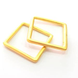 以下が含まれることがあります： 2つの正方形の金色のフープが、片方がもう片方よりわずかに大きい状態で、互いに重ねられています。