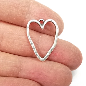 May include: Silver-toned metal heart charm with a hammered texture. The heart is open and has a loop at the top for attaching to jewellery or other crafts.