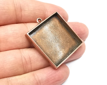 May include: A square copper-toned metal pendant with a square opening for a resin or glass insert. The pendant has a loop at the top for attaching a chain or cord.