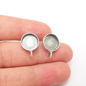 May include: Two silver-toned round pendant trays with a loop for hanging. The trays are designed for resin crafting and have a smooth, shiny surface.