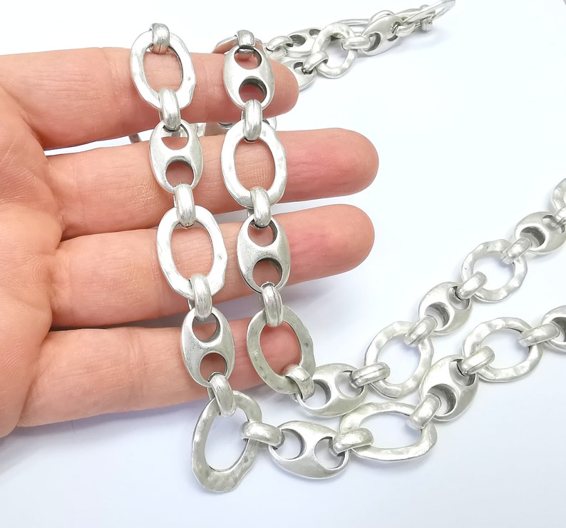 May include: A silver chain with oval links. The chain is made of metal and has a hammered finish. The chain is about 18 inches long.