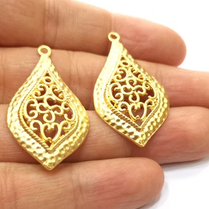 May include: Two gold filigree teardrop shaped pendant charms with a hammered texture. The charms have a delicate, intricate design.