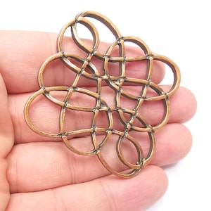 May include: A large, intricate, copper-colored metal pendant with a geometric design. The pendant is shaped like a flower with multiple overlapping circles and loops.