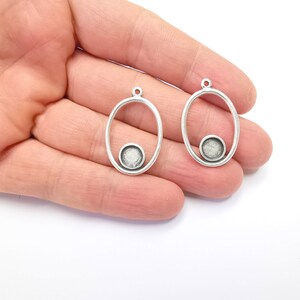 May include: Two silver oval-shaped pendant charms with a smaller circle cut out in the center. The circles have a textured silver finish.