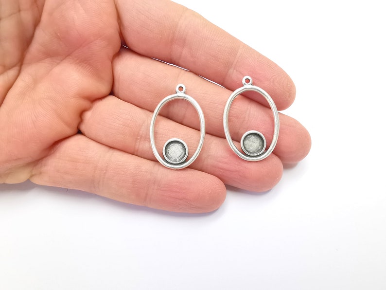 May include: Two silver oval-shaped pendant charms with a smaller circle cut out in the center. The circles have a textured silver finish.