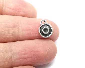 May include: Silver charm with a round, concentric circle design. The charm has a loop at the top for attaching to a necklace or bracelet.