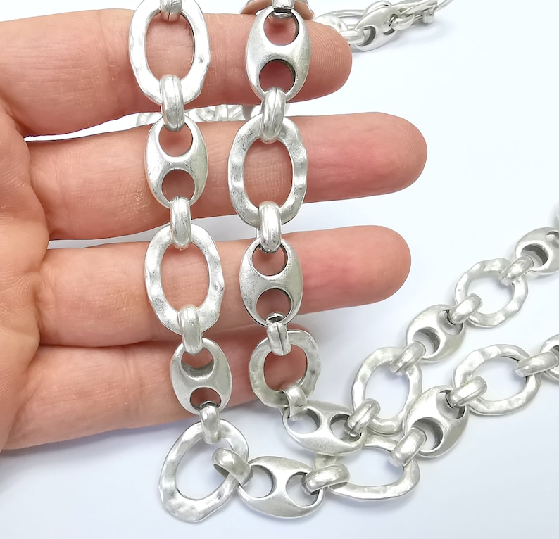 May include: A silver chain necklace with large, oval-shaped links. The chain is made of metal and has a textured finish.