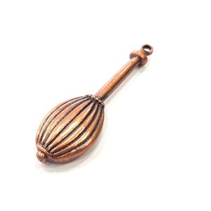 Könnte beinhalten: Ein kupferfarbener Metallanhänger mit einer länglichen, gerippten ovalen Form und einem schmalen Stiel. Der Anhänger hat oben eine kleine Schlaufe zum Befestigen. Das Design ist detailliert und von Vintage-Inspiration. Ca. 4 cm lang.