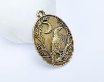 Op de afbeelding: Een gouden metalen hanger met een gedetailleerd ontwerp van een raaf die op een tak zit met een halve maan op de achtergrond.