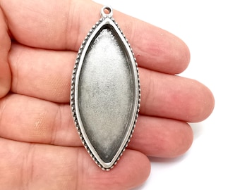May include: A silver-toned, teardrop-shaped pendant tray with a beaded edge. The pendant has a loop at the top for attaching to a chain or cord. The tray is designed to hold a cabochon or other decorative element.
