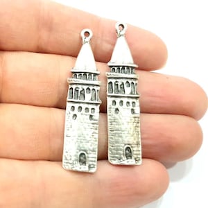 Puede incluir: Dos colgantes de plata con forma de torre con techo puntiagudo y ladrillos detallados.