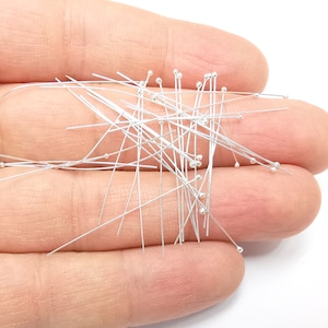 May include: A large pile of silver head pins with round heads. The pins are scattered and overlapping.