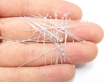 May include: A large pile of silver head pins with round heads. The pins are scattered and overlapping.