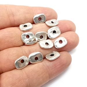 May include: A group of silver-toned metal beads with a hole in the center of each bead. The beads are oval-shaped and have a slightly textured surface.