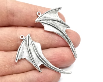 May include: Two silver-toned metal wings with a loop at the top for attaching to jewelry or crafts. The wings are detailed with a textured surface and have a slightly curved shape.