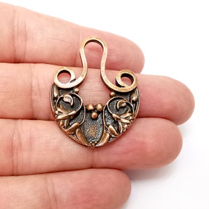 May include: A copper-toned metal charm with a decorative floral design and a loop at the top. The charm is in the shape of a horseshoe with a stylised floral pattern.