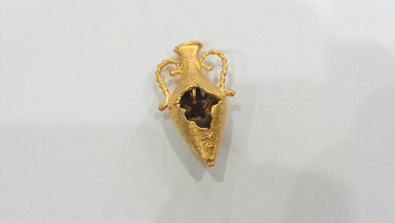May include: A gold-colored, broken, decorative vase with two handles. The vase is in the shape of a heart and has a textured surface.