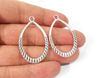 May include: Two silver oval-shaped pendant charms with a textured design. The charms have a small loop at the top for attaching to jewellery.