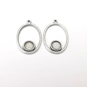 May include: A pair of silver oval-shaped earrings with a small round silver charm in the center of each oval.
