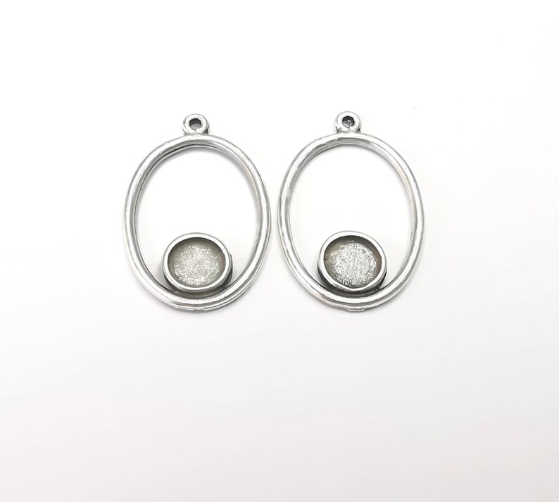 May include: A pair of silver oval-shaped earrings with a small round silver charm in the center of each oval.