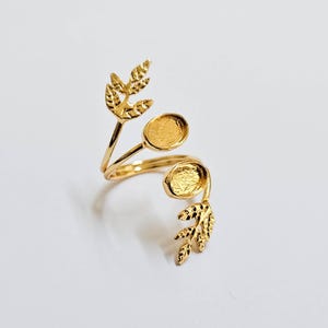 May include: A gold ring with a leaf design. The ring has two circular settings and leaf accents. The ring wraps around the finger, with leaf details at the top and bottom. The ring is made of gold.