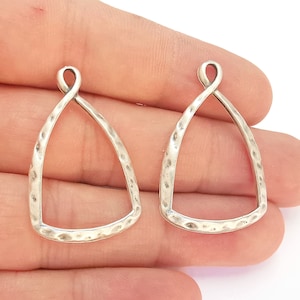 Puede incluir: Dos blanks de pendientes de metal plateado con textura martillada y forma triangular. Los blanks tienen un bucle en la parte superior para sujetar los hilos de los pendientes.
