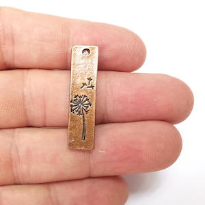 May include: A copper-colored metal charm with a dandelion design. The charm has a hole at the top for attaching to a necklace or bracelet.