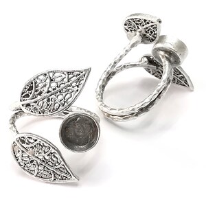 Puede incluir: Anillo de plata con dos diseños de hojas y un engaste redondo. El anillo es ajustable y se puede llevar en diferentes dedos.