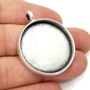 May include: Silver round pendant with a smooth, white surface and a loop at the top for attaching a chain.