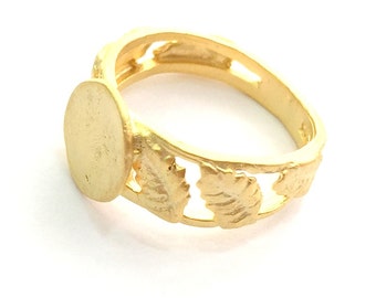 Op de afbeelding: Een gouden ring met een rond, plat middenstuk en een ontwerp van bladeren rond de band.