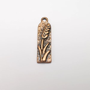 May include: A copper-toned metal charm with a wheat stalk design. The charm is rectangular and has a textured surface.