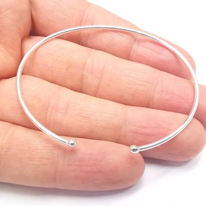 May include: A simple silver bangle bracelet with rounded ends. The bracelet is open and has a smooth, polished finish.