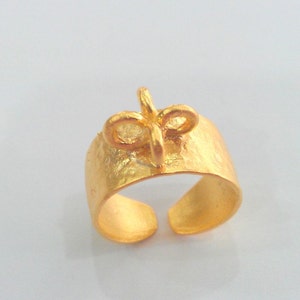 May include: A gold ring with a textured band and a bow-shaped design on top.